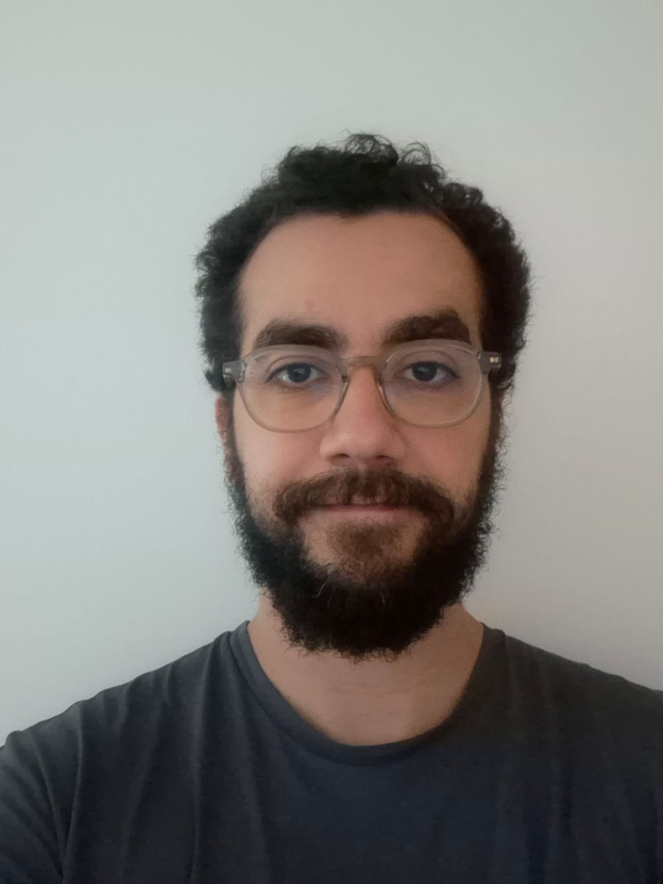 Foto que apresenta a do professor Eduardo Georjeão estilo foto 3x4. Ele é um homem pardo de pele em tom mais claro com barba completa com bigode e óculos arredondados. Olhos castanhos escuros e cabelos crespos de cachos abertos e cortado bem curto.